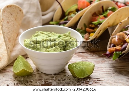 Tacos and tasty guacamole in bowl on light wooden background, closeup