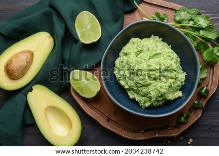 Bowl with tasty guacamole, avocado and lime on dark wooden background, closeup