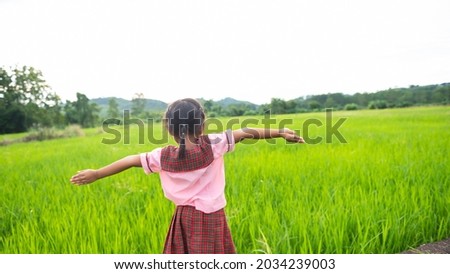 A girl in school uniform spreads her arms in the middle of a golden yellow rice field. girl student coming back from school