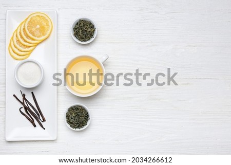 Cup of hot tea, bowls with dry leaves and lemon on wooden background