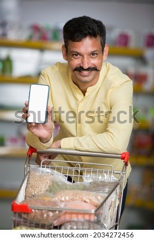 Portrait of happy man showing mobile phone screen at supermarket Royalty-Free Stock Photo #2034272456