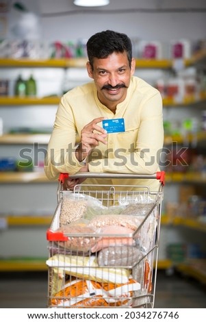 Happy young man holding credit card at grocery store. Royalty-Free Stock Photo #2034276746