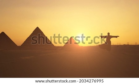 Female traveller looks to the silhouette of pyramids at the sunset in the desert. Aerial shot. Royalty-Free Stock Photo #2034276995