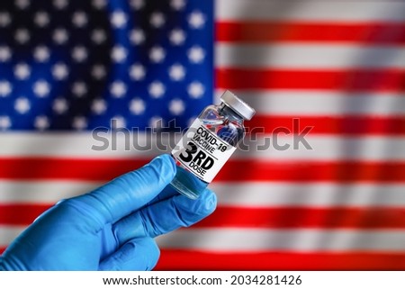 Third dose vaccine for Covid-19 for booster shot in the risk population diseases in United States. Doctor with a vial with 3rd dose of the vaccine for covid-19 or Coronavirus in front of the USA flag Royalty-Free Stock Photo #2034281426