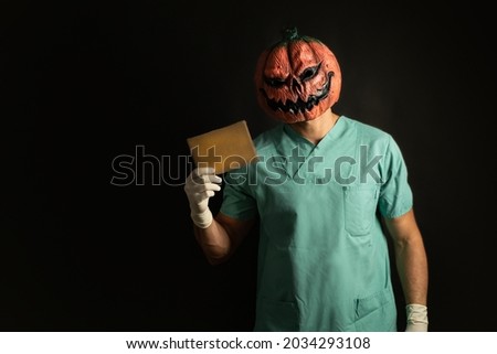 Nurse Doctor, wearing a Halloween mask, holding a sign with copy space, in front a black background. Royalty-Free Stock Photo #2034293108