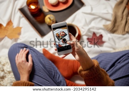 people, technology and leisure concept - young woman with smartphone taking picture of autumn set at home