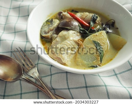 Thai green curry with chicken (Gaeng Kiaw Wan Gai or Gaeng Keow Waan Kai) served in white bowl on grid fabric background with fork and spoon. Popular delicious dish in Thailand theme (selective focus)