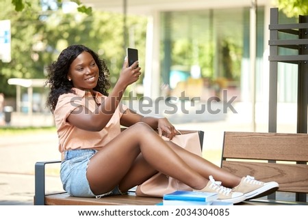 education, school and people concept - happy smiling african american student girl taking selfie with smartphone sitting on bench in city