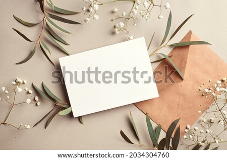 Greeting or invitation card mockup with craft paper envelope, eucalyptus and gypsophila twigs. Card mockup with copy space on beige background.