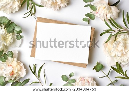 Invitation or greeting card mockup with envelope and white peony flowers with eucalyptus twigs on white background