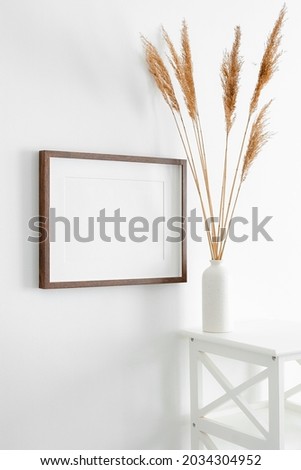 Horizontal wooden frame mockup for artwork, photo, print and painting presentation. White walll with vase and dry grass decorations. Minimalistic interior design.