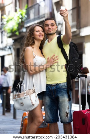 Happy man and woman with luggage doing selfie during city tour 