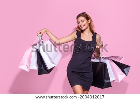 young woman in a black dress holds shopping bags and emotionally raised up hands on a pink background, Black Friday, shopping