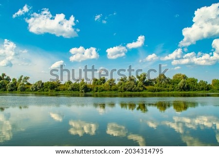 River surface with forest on the opposite side. Reflection of trees and sky with clouds in the water. Idyllic picture of nature.