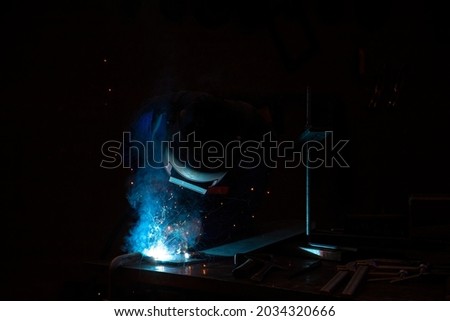 Welder welding metal in workshop with sparks. Welding steel on site at a engineering site. The sparks from the arc light the welding shield helmet.