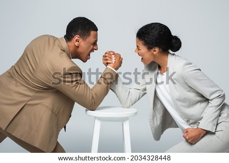 side view of african american businesswoman and man doing arm wrestling on white chair isolated on grey