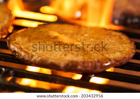 Hamburger patties on a grill with fire under. Selective focus
