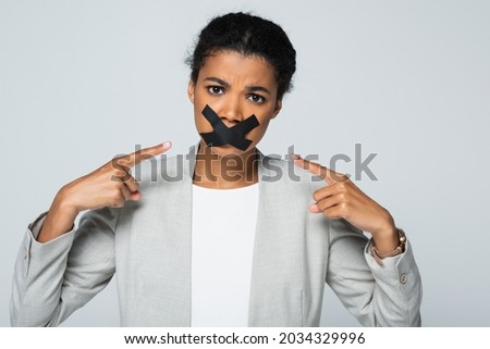 african american businesswoman pointing at scotch tape on mouth isolated on grey