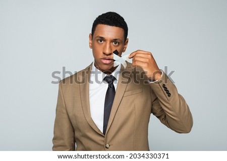 african american businessman taking off scotch tape on mouth isolated on grey
