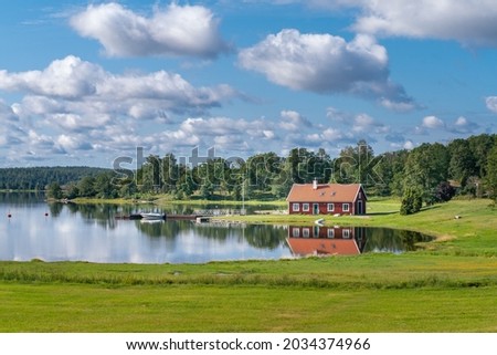 Typical red wooden house in countryside by the sea in natire of southern Sweden on a beautiful sunny summer day. Relaxing rural landscape. Reflection on water surface. Holiday in Sweden. Royalty-Free Stock Photo #2034374966