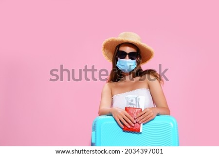 Young woman waiting for flight, sitting on floor near her suitcase, wearing face mask and sunglasses to prevent coronavirus.