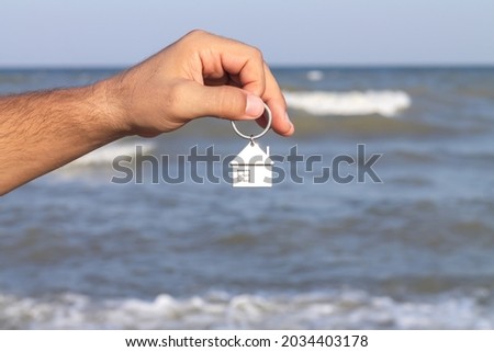 Man holding key with keychain to new home or apartment on sea background. Rent, mortgage or investment concept