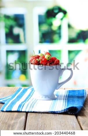 Forest berries in cup, on wooden table, on bright background