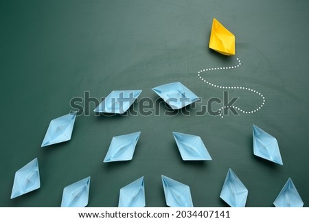 group of blue paper boats are sailing in one direction, one yellow is sailing in the opposite direction. The concept of an extraordinary personality, to act contrary to the foundations of society