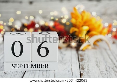 White wood calendar blocks with the date September 6th and autumn decorations over a wooden table. Selective focus with blurred background. Labor Day.