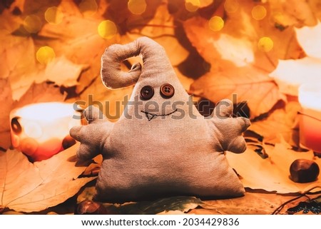 Toy monster with button eyes among autumn leaves. Halloween holiday card and home decoration with blurred lights bokeh