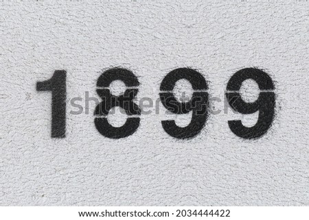 Black Number 1899 on the white wall. Spray paint. Number one thousand eight hundred and ninety nine.