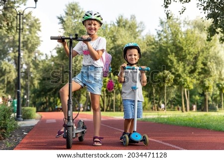 Portrait of two cute blond little caucasian sibling kids girl wear safety helmet enjoy having fun riding electric scooter city street park outdoors sunny day. Healthy sport children activity outside Royalty-Free Stock Photo #2034471128
