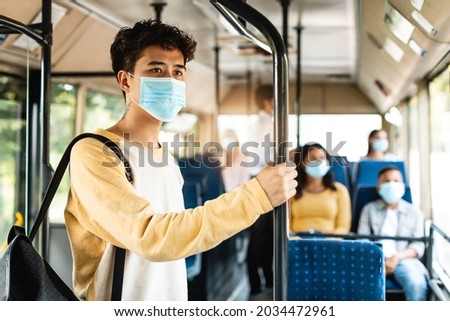 Modern Travel Transportation. Portrait of asian male passenger in disposable medical mask holding on handrails in urban bus. Concept of city trip in context of covid pandemic, cororna virus quarantine Royalty-Free Stock Photo #2034472961