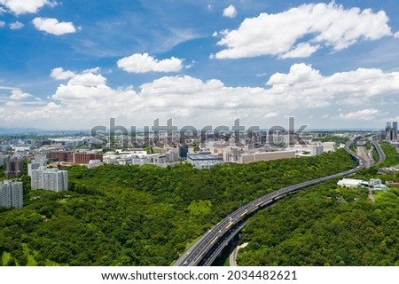 The highway cross the green forest and city in LinKou, New Taipei City under blue sky. Famous city in North Taiwan, Asia. Aerial view of highway and cityscape.
