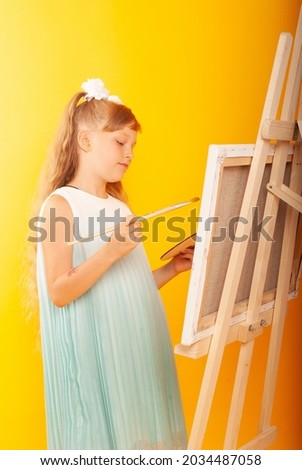 girl artist who draws in a turquoise dress with space for text isolated on a yellow background