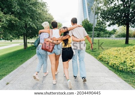 Back view of group of multiethnic friends hugging walking outdoor bonding and socialising Royalty-Free Stock Photo #2034490445