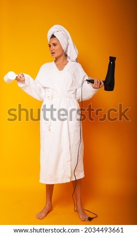 A girl of 30 years thought about opening her mouth with a cup in her hands and a hairdryer on a yellow background with space for text.