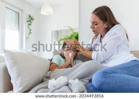 Mother measuring temperature of her ill kid. Sick child with high fever laying in bed and mother holding thermometer. Hand on forehead. Royalty-Free Stock Photo #2034493856