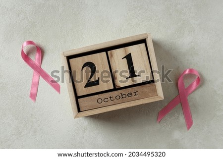 Pink awareness ribbons and wooden calendar with 21 October on white textured background