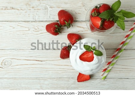 Glass of strawberry milkshake and ingredients on white wooden table