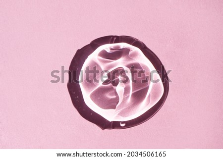 Round transparent drop of hyaluronic acid gel on a pink background close-up. Top view, place for text.
