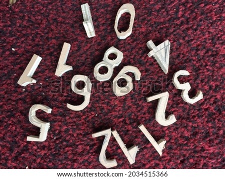 Close up of numbers hand made created by crafting ply wood with fret saw, in a jumbled group against background of red carpet ready to make clock face numerical time shapes