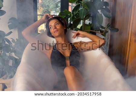 Woman relaxing in round outdoor bath with tropical flowers, organic skin care, luxury spa hotel, lifestyle photo. With smoke in the bathroom.