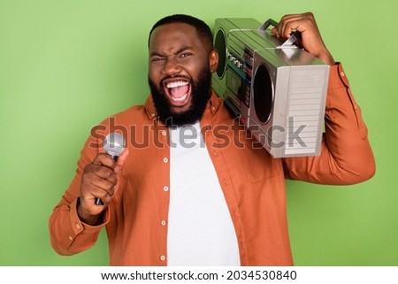 Photo of funny young brunet guy sing hold boom box wear orange shirt isolated on green color background