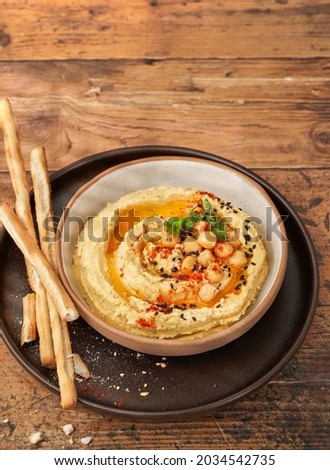 Chickpea hummus in bowl with breadsticks on wooden table. Top view, copy space, selective focus.