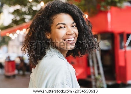 Smiling african-american woman young student freelancer walking in city park cafe outdoors. Beautiful teenager with toothy smile. Royalty-Free Stock Photo #2034550613