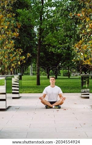 Young man wearing sportswear practicing yoga in the park. Man sit in lotus position and meditate during sunrise between mirrors.