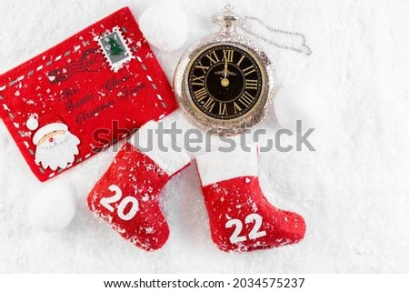 New Year 2022. New Year's clock. Red Boots of Santa Claus in the snow. Christmas boot.  Chimes. Letter to Santa. Card. Photo