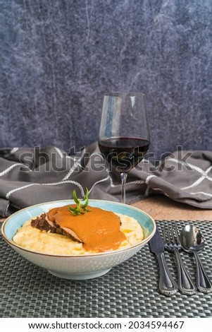 Vertical picture of an elegant table with a plate of cornstarch with roasted beef served with red wine