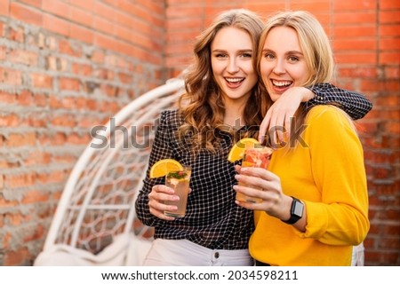 Two young women drinking healthy drinks outdoors. Happy female friends with citrus cocktails on the roof party